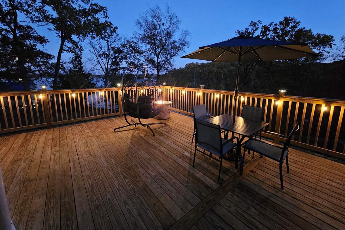 Spacious nighttime deck with café seating, glowing string lights, and serene lake views — perfect for relaxing under the stars