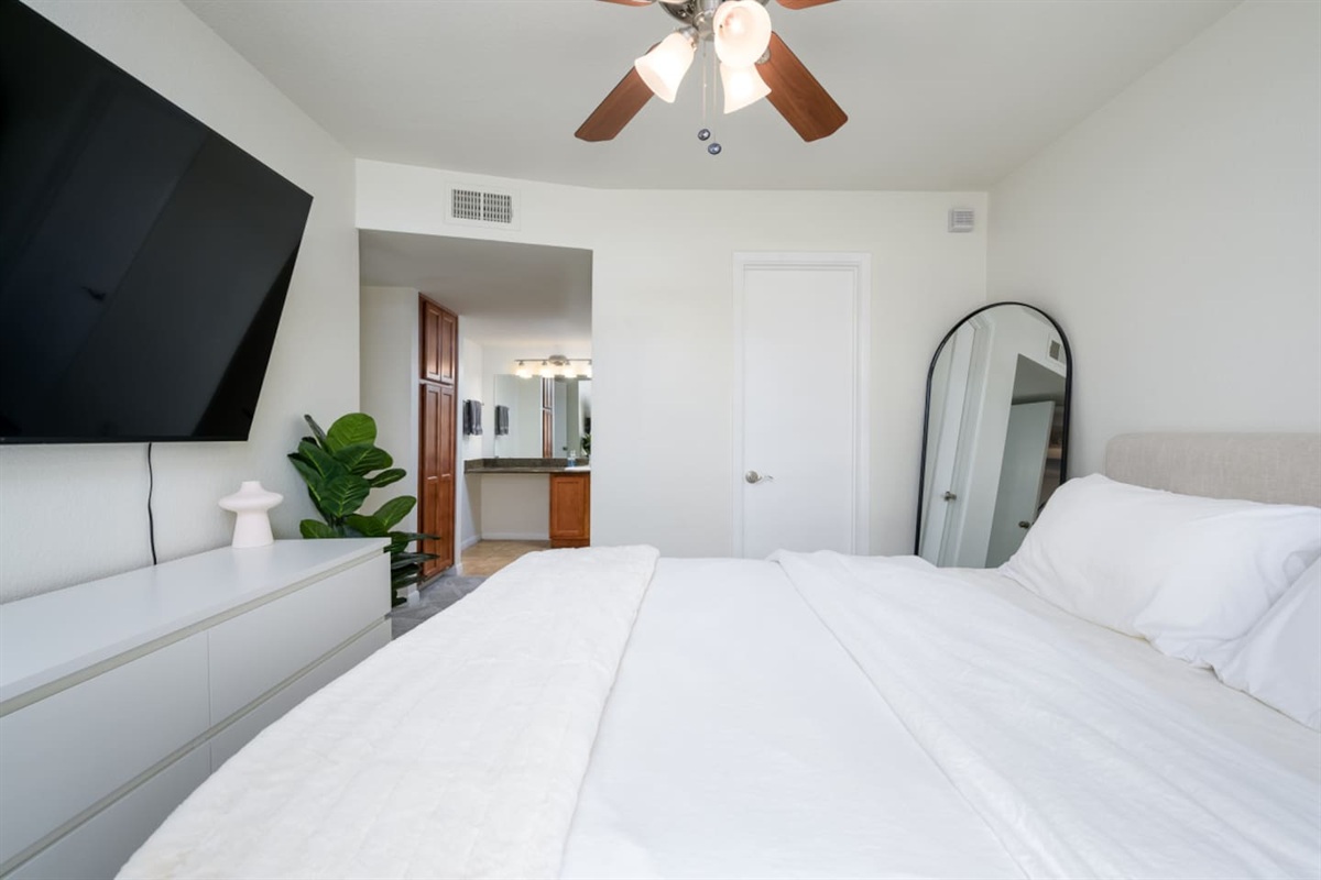 Bedroom with queen bed, wall-mounted TV, ceiling fan, and simple storage for everyday comfort.
