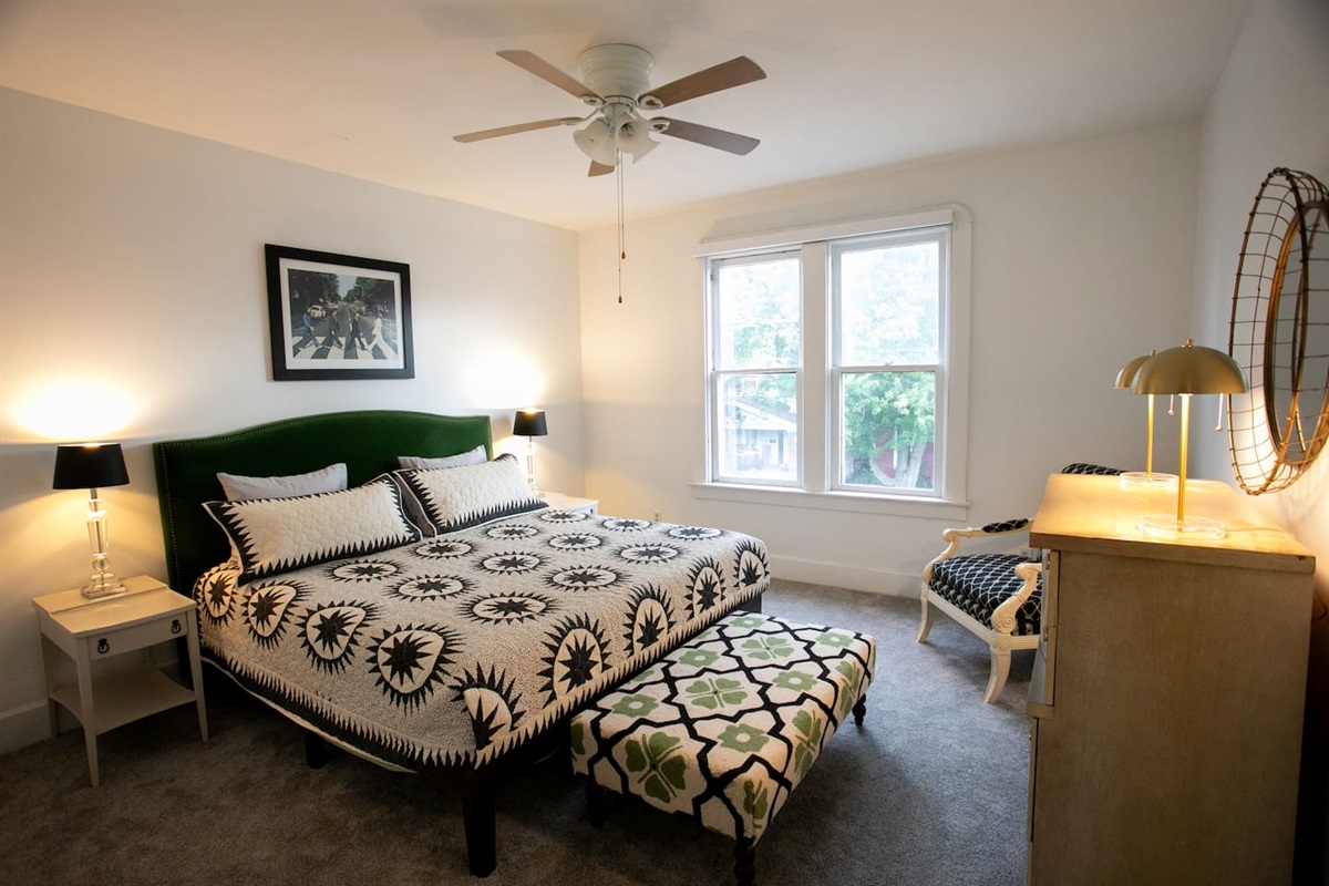 Spacious king bedroom with ceiling fan for steady airflow, a personal bedside fan, and convenient wireless charging — thoughtfully curated for comfort, ease, and a true at-home feel.