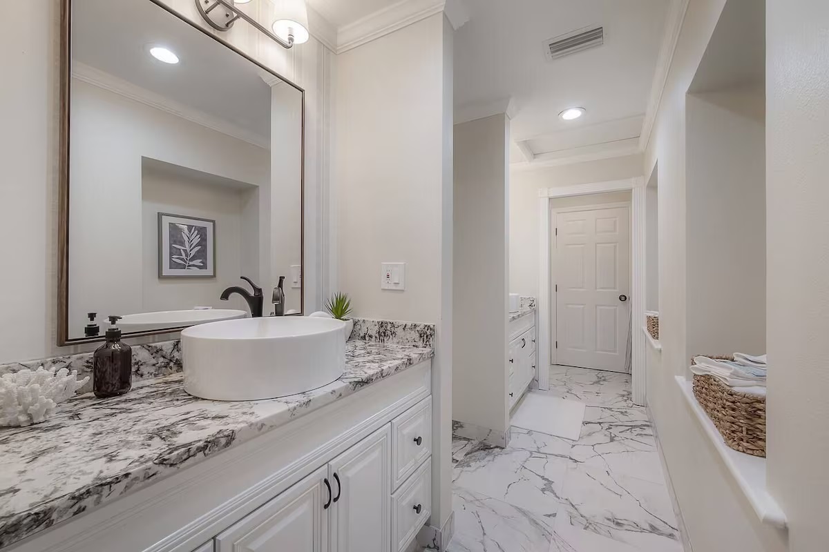 A bright and elegant bathroom featuring marble-style tile floors, dual vanities with granite countertops, and modern vessel sinks.