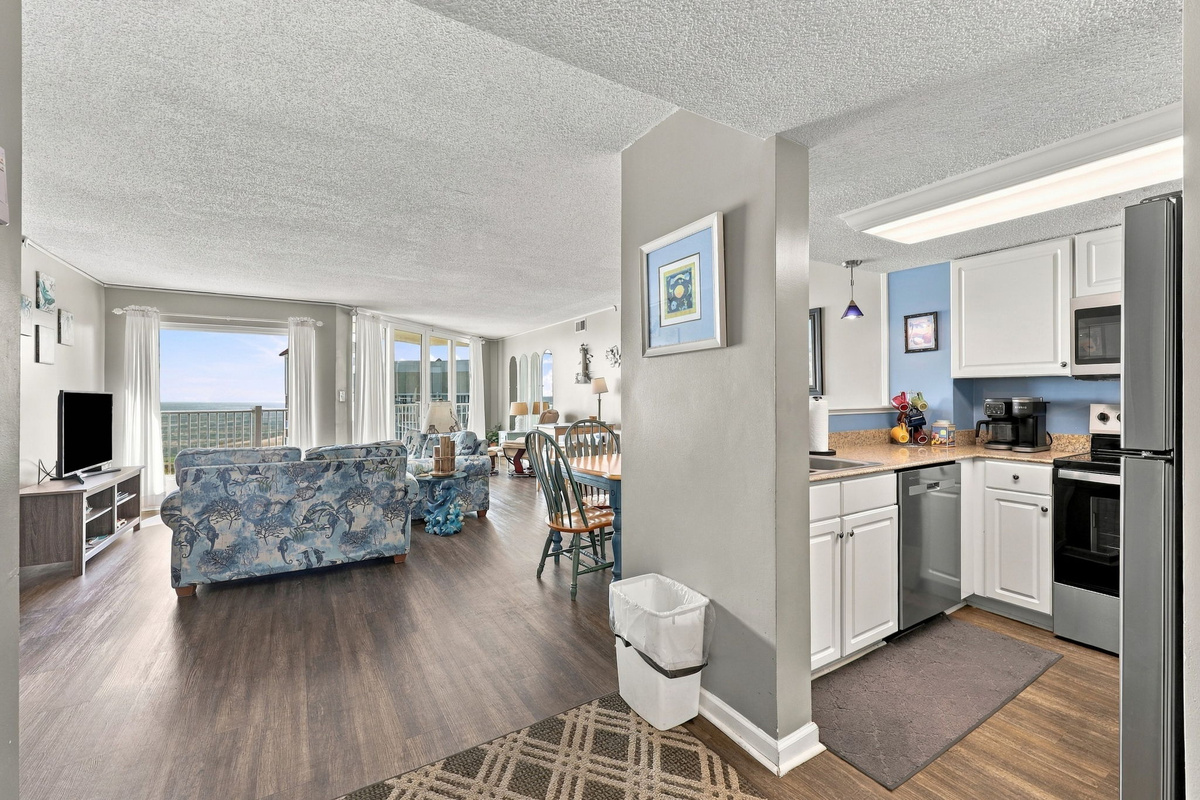 Bright, open-concept living area with wood-look flooring, showing the cozy seating area and full kitchen layout.