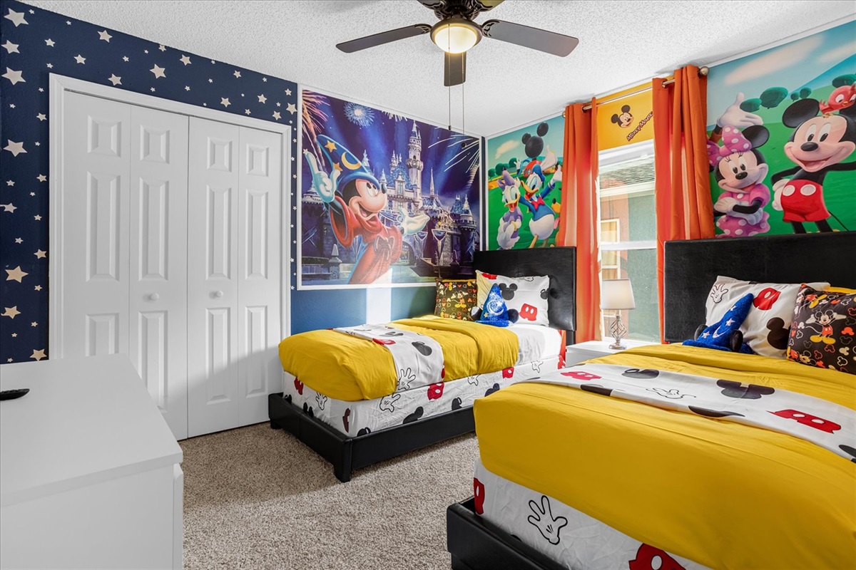 A colorful kids' bedroom featuring 2 twin beds with Mickey Mouse-theme and vibrant wall murals.