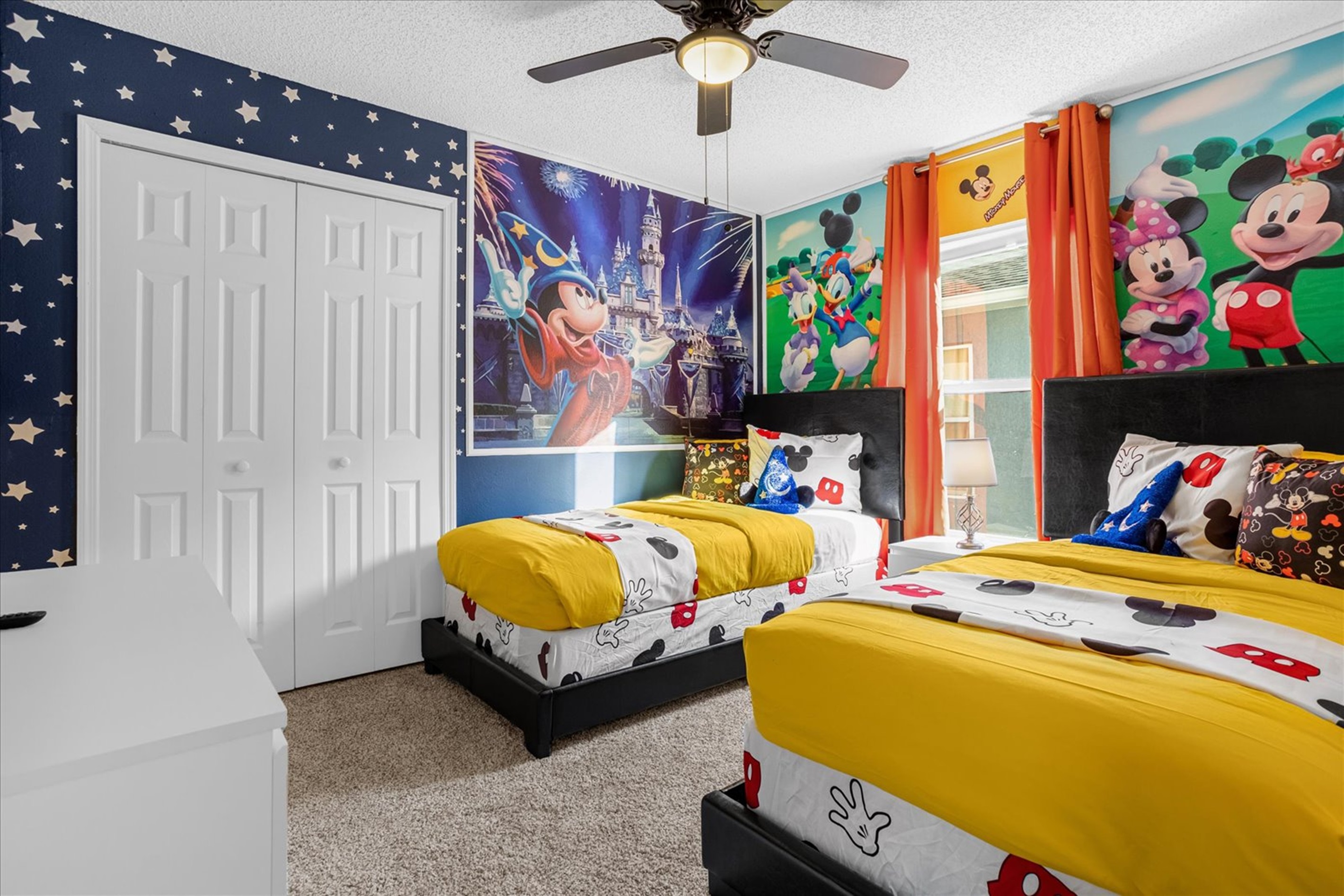 A colorful kids' bedroom featuring 2 twin beds with Mickey Mouse-theme and vibrant wall murals.