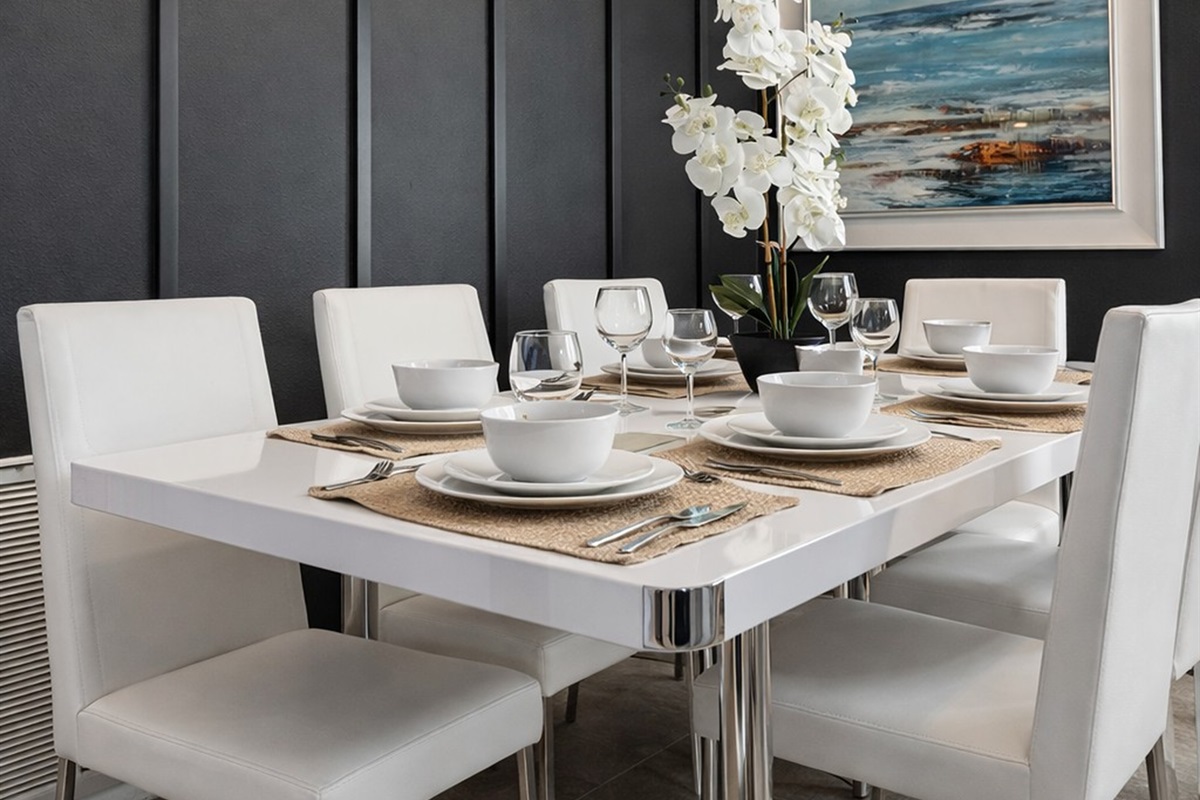 Modern dining area with a sleek white table set for four and a coastal-themed painting.
