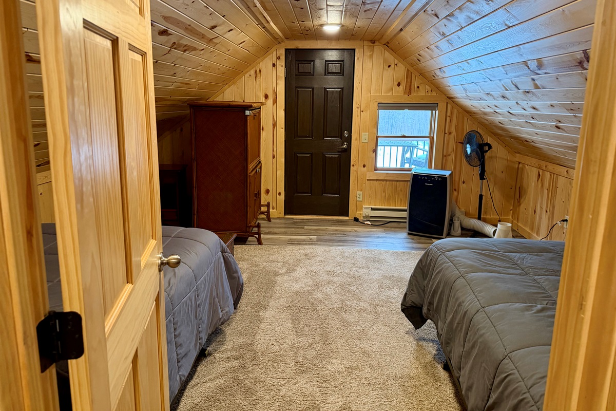 Passing through the first upstairs bedroom on your way to the second, you’ll spot the door to the outdoor deck plus the mobile A/C and a fan, everything you need to stay cool and comfortable in this quaint, cozy sleeping space.