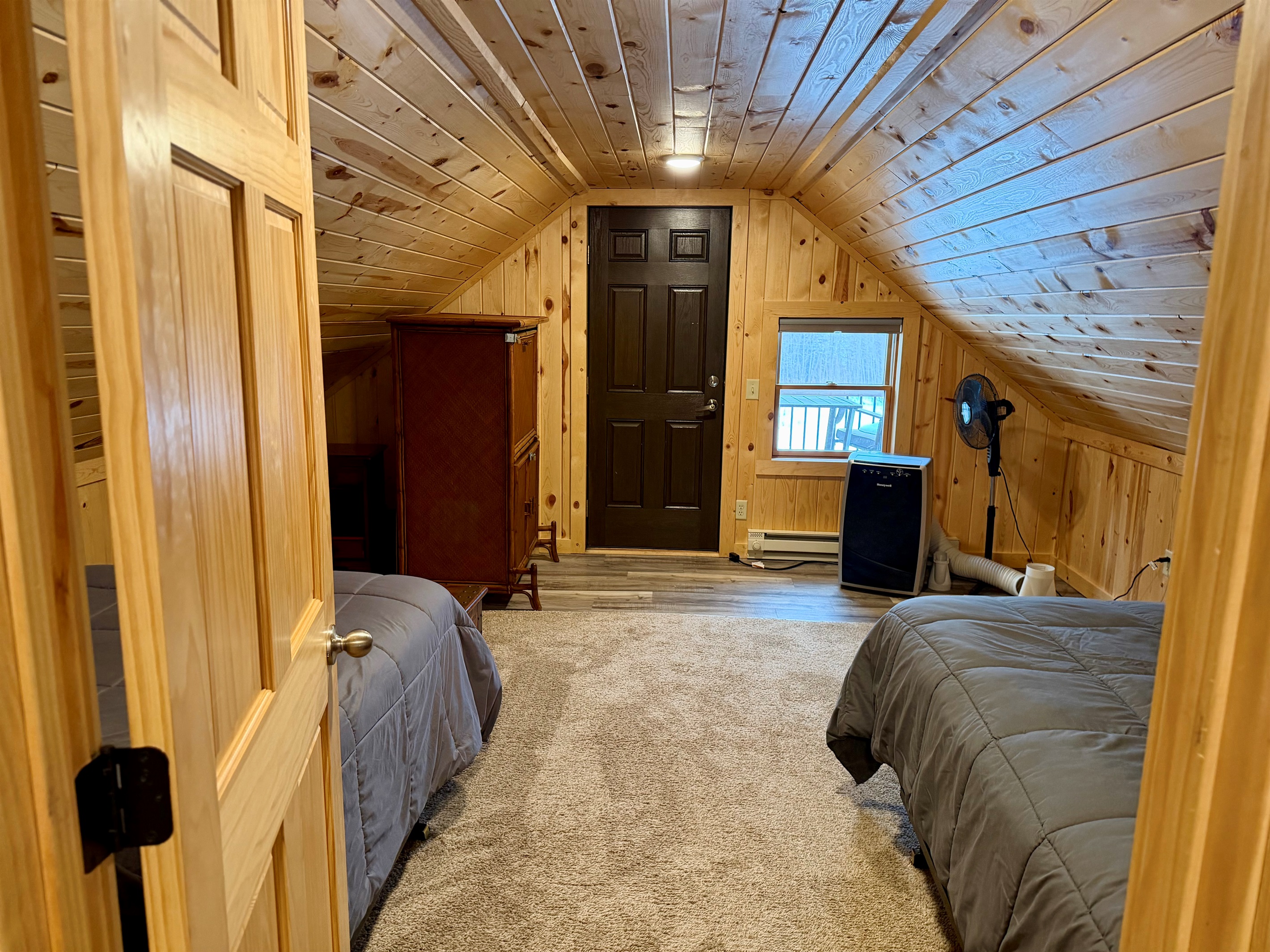 Passing through the first upstairs bedroom on your way to the second, you’ll spot the door to the outdoor deck plus the mobile A/C and a fan, everything you need to stay cool and comfortable in this quaint, cozy sleeping space.