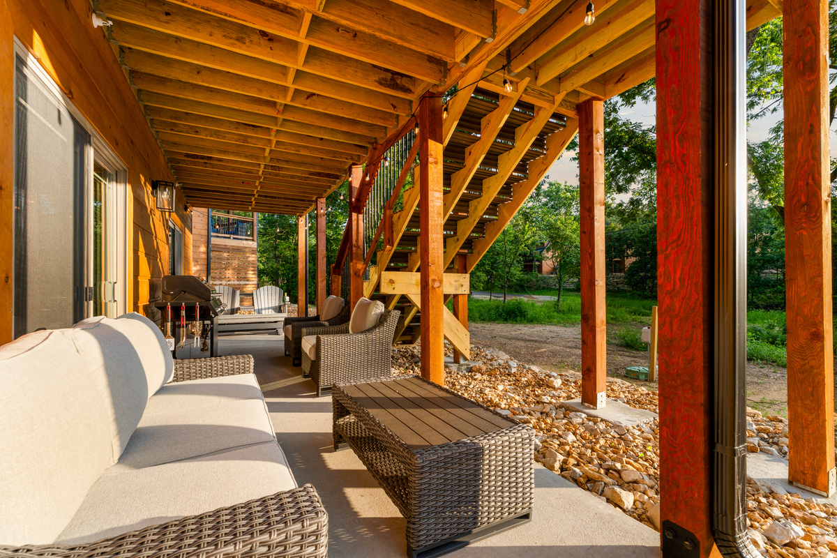 A second living room outdoors — cushioned wicker seating and a grill under the deck.
