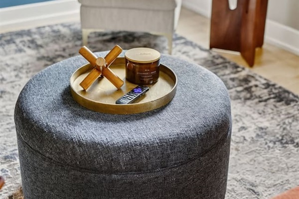 Unwind in a stylish living room featuring a modern accent chair, cozy ottoman with designer décor, and a calming blue wall. Perfect for relaxing with a glass of wine or streaming your favorite shows after exploring downtown Des Moines.