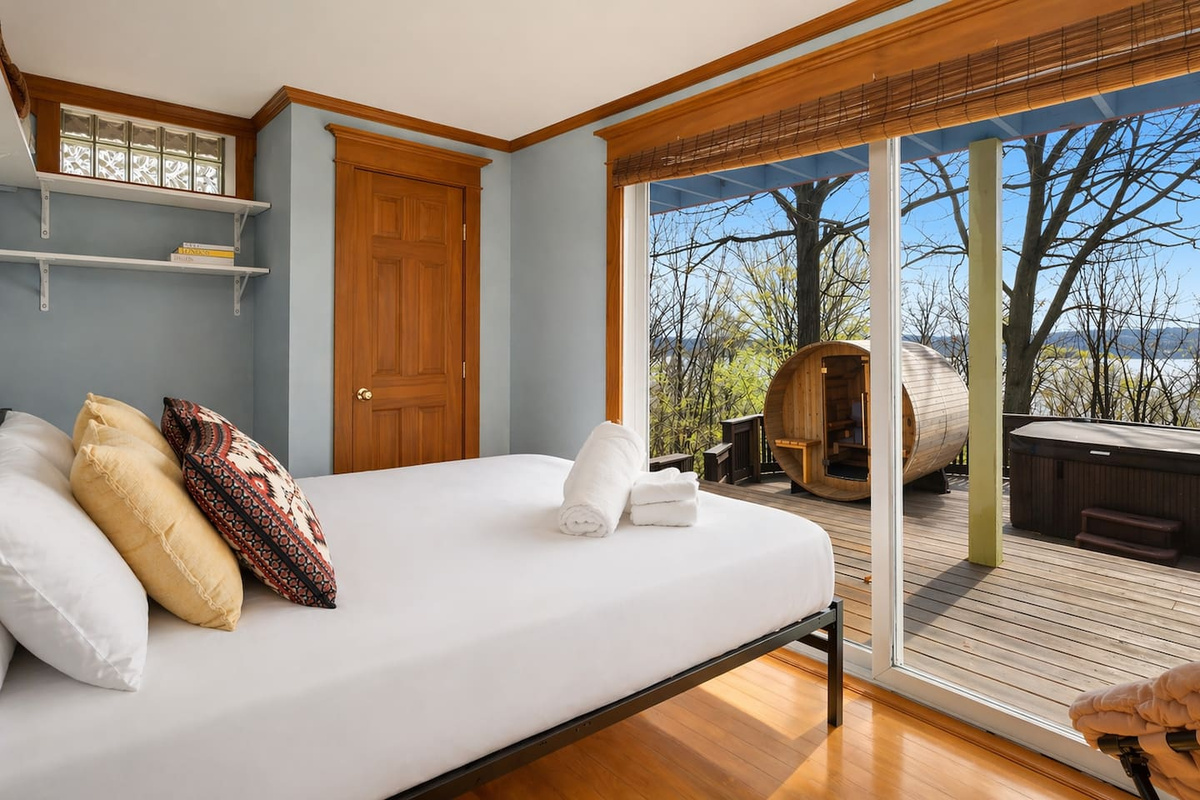 “Enjoy this bright downstairs bedroom featuring a glass door with direct access to the balcony, hot tub, and spa. Relax in comfort with soft bedding and natural light, while vintage suitcase décor adds a charming touch of travel-inspired style.”