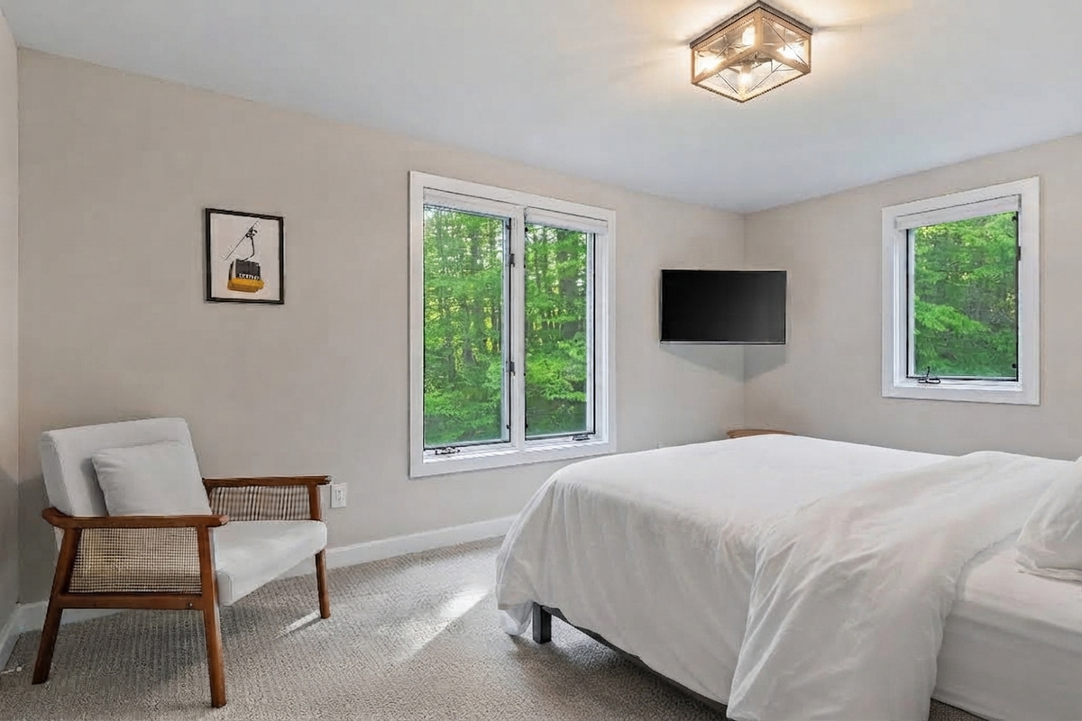 Guest bedroom with queen bed, TV and armchair overlooking the Vermont treeline