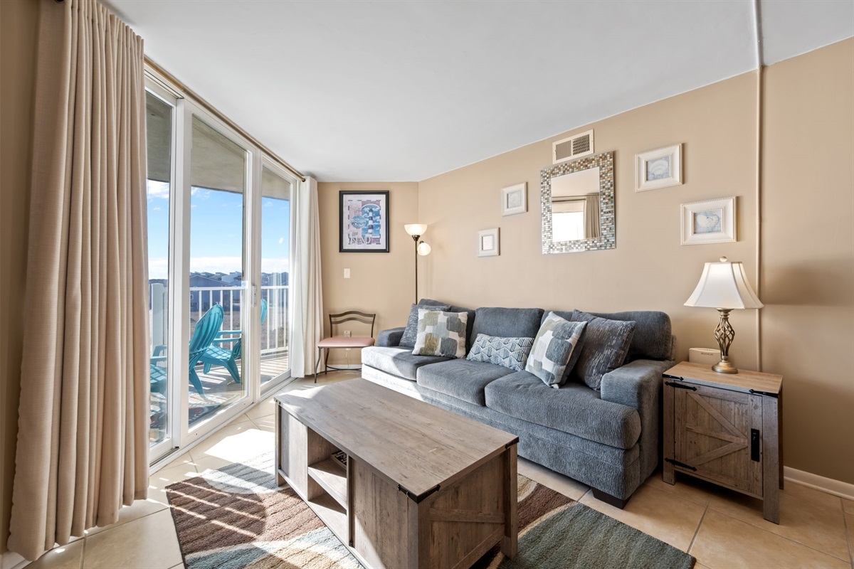 Sun-filled living space with a comfortable sofa, coffee table, and floor-to-ceiling sliding doors leading to the oceanfront balcony