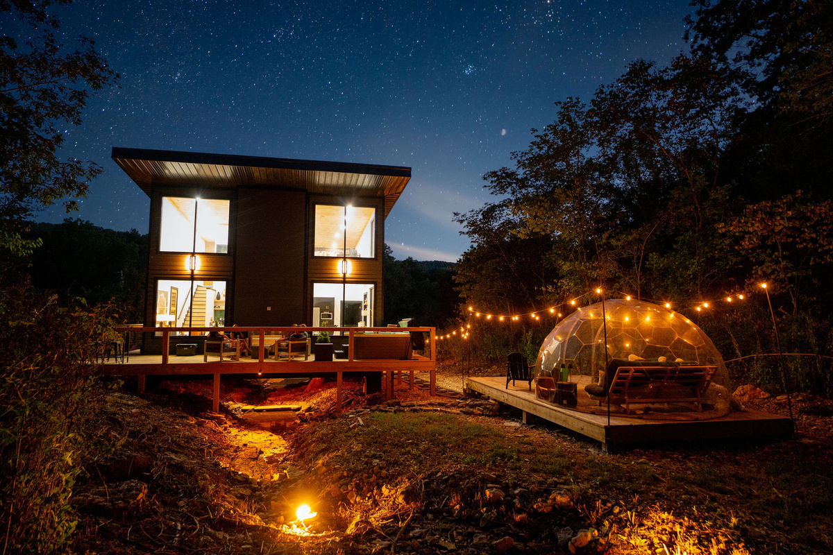 Your private Ozark retreat after dark—glass cabin, stargazing dome and firelight tucked into the woods.