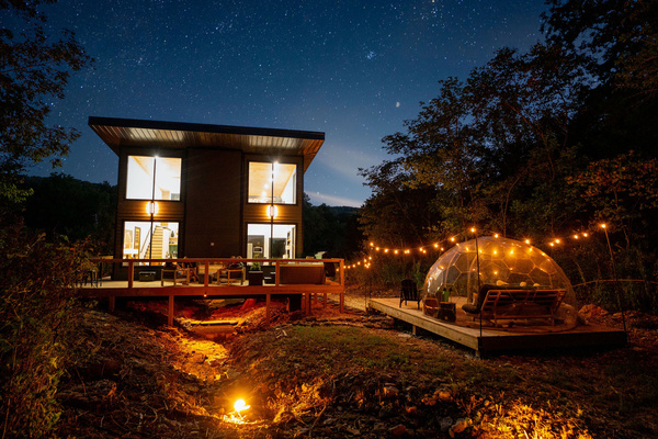 Your private Ozark retreat after dark—glass cabin, stargazing dome and firelight tucked into the woods.