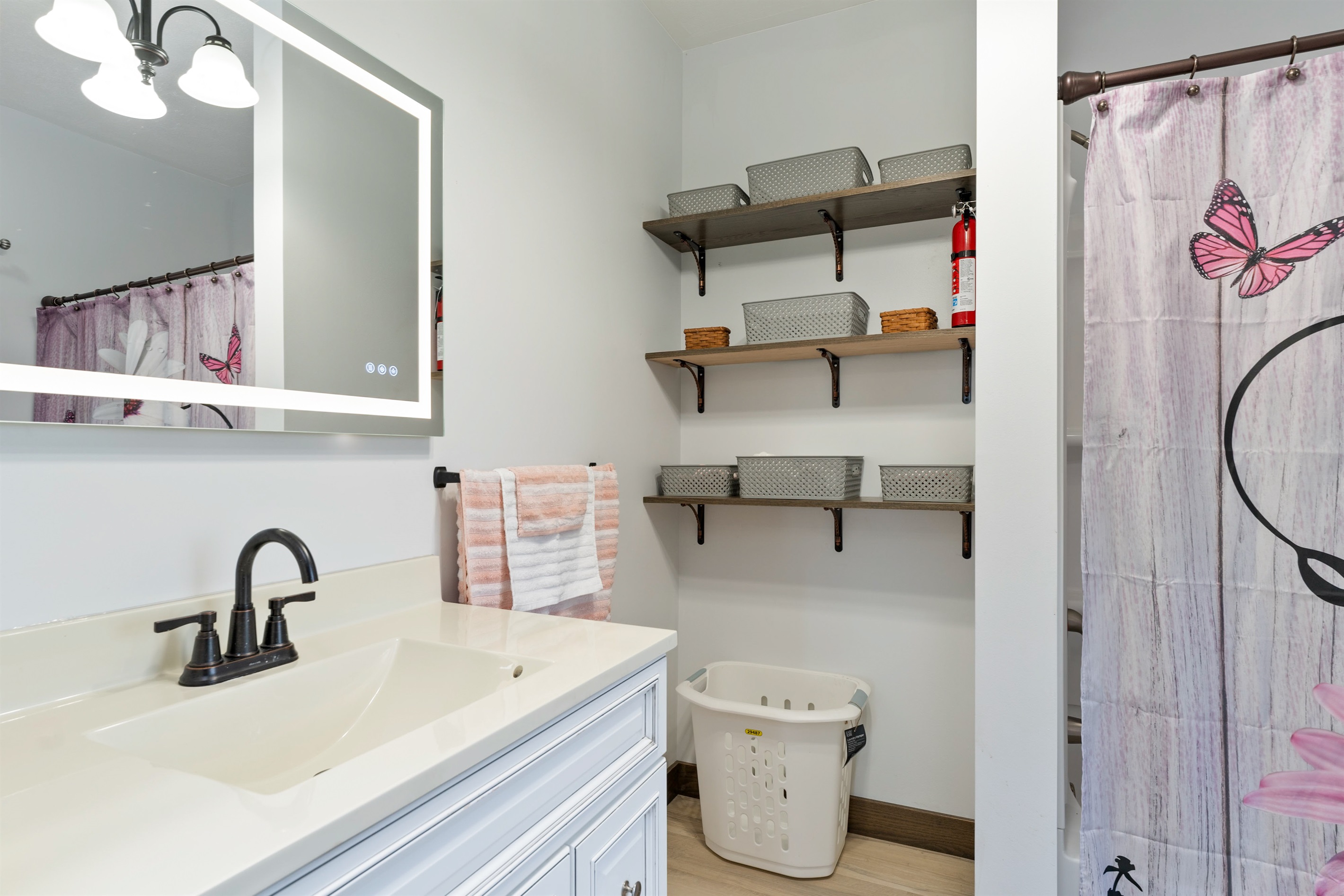 Modern vanity with sleek black fixtures, backlit mirror, and open shelving for stylish storage—bringing both function and charm to this refreshed full bathroom upstairs.