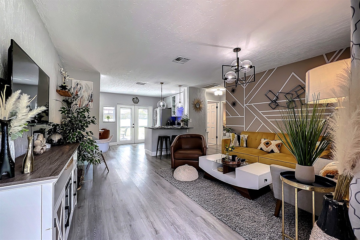 Stylish living room with accent wall, yellow sofa, and modern decor; open to kitchen area.