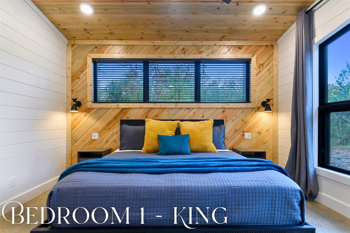 Bedroom 1 features a king bed, wood-paneled accents, and large windows for natural light and calming forest views.