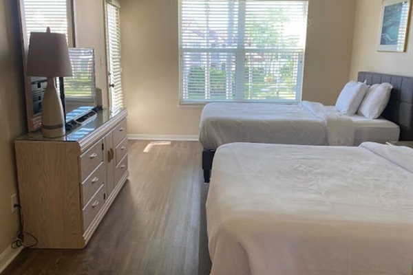 Comfortable bedroom with two beds, dresser storage, TV, wood-look flooring, and natural light.