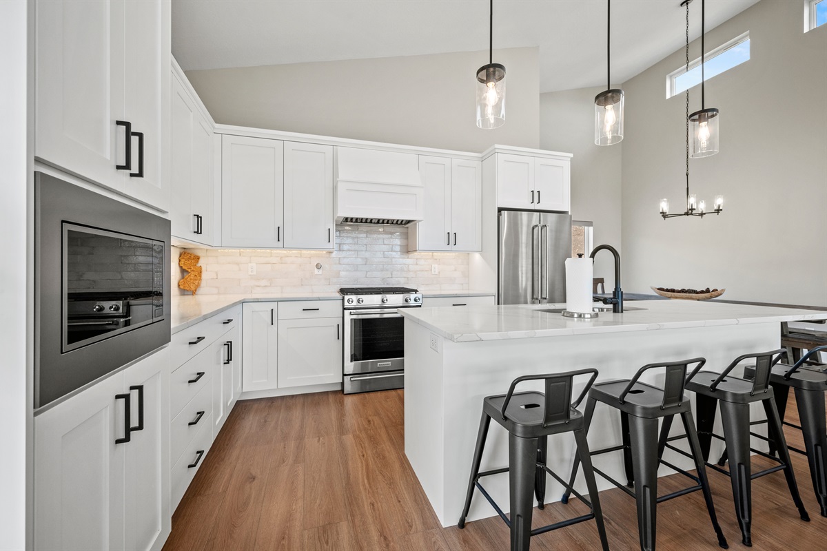 Built-in microwave, chic island lighting, and white cabinetry create a fresh, modern kitchen.