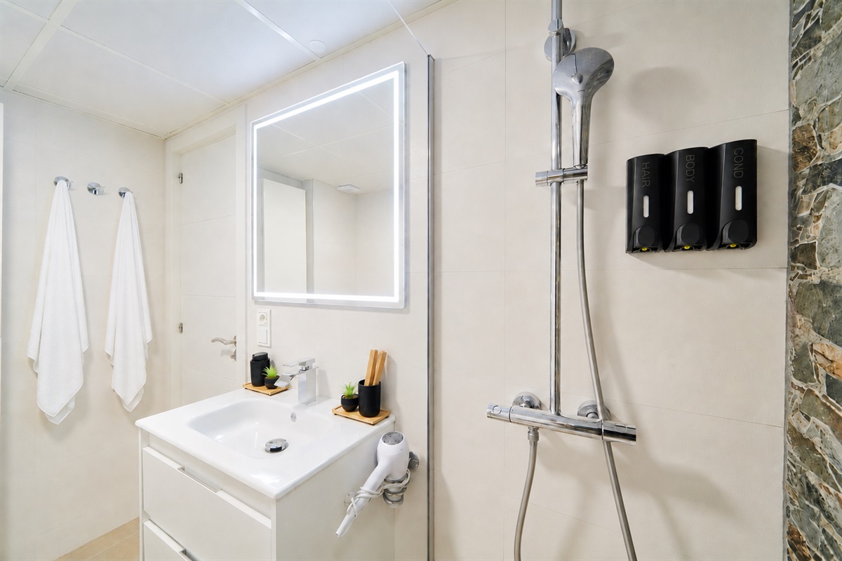 Modern bathroom with walk-in rain shower, stone accent wall, LED mirror, and fresh spa-like touches for your comfort.