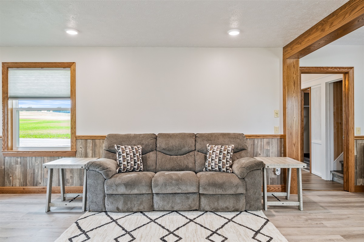 Cozy up in this inviting living room featuring a plush reclining sofa, stylish accent pillows, and rustic wood trim with countryside views—perfect for relaxing after a day of exploring.