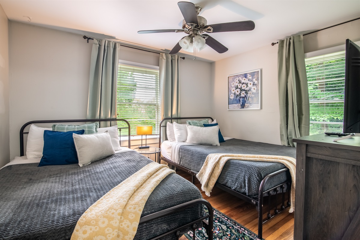 Spacious twin bedroom with double windows, blackout curtains, and calming decor for a peaceful night’s sleep.