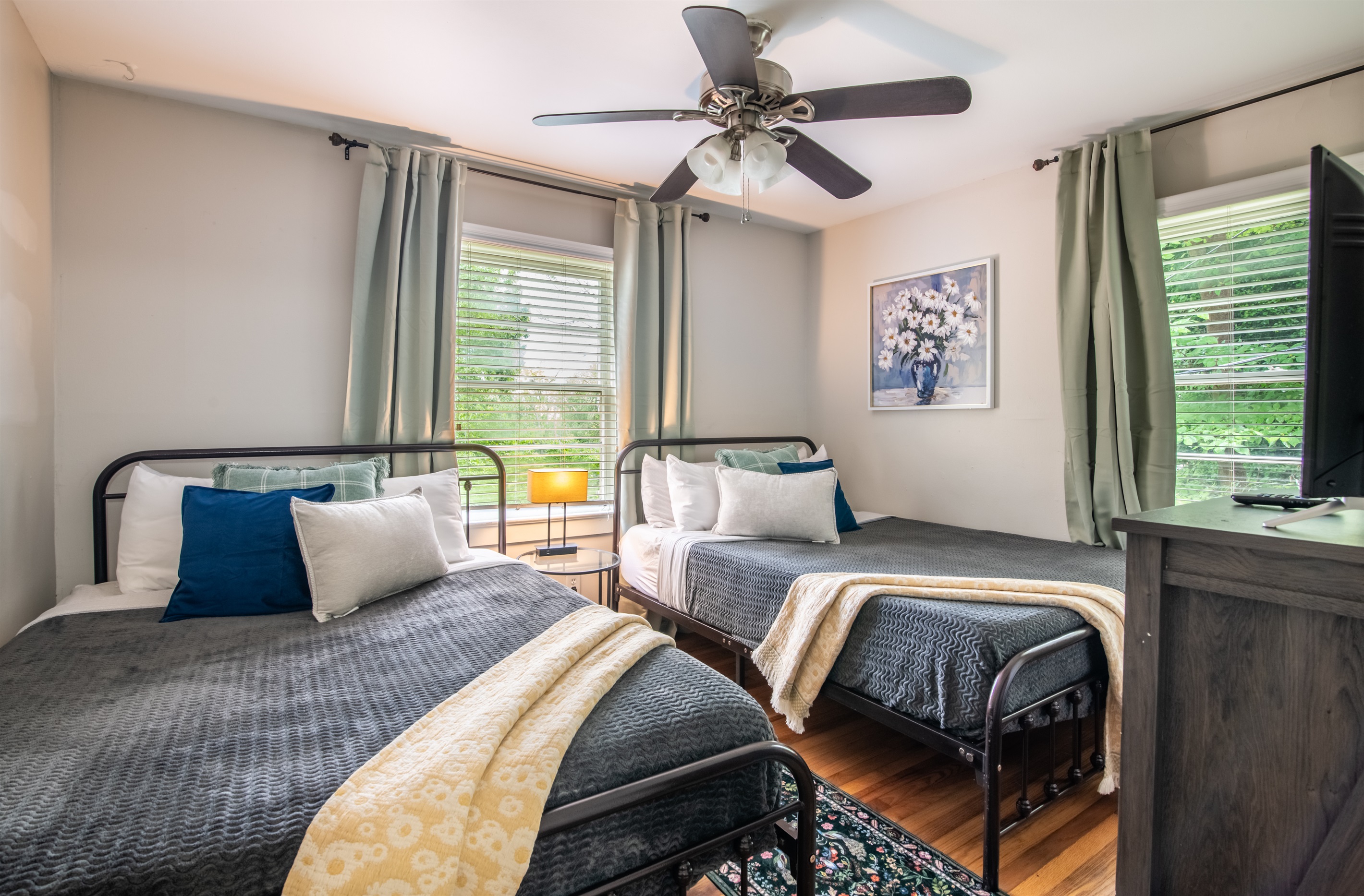 Spacious twin bedroom with double windows, blackout curtains, and calming decor for a peaceful night’s sleep.
