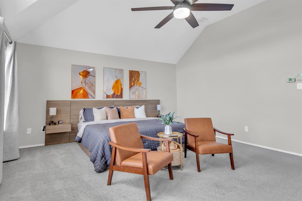 Thoughtfully designed primary bedroom with a king bed, cozy seating area, ceiling fan, blackout shades, modern art accents, high-speed Wi-Fi, and climate comfort ideal for longer stays.