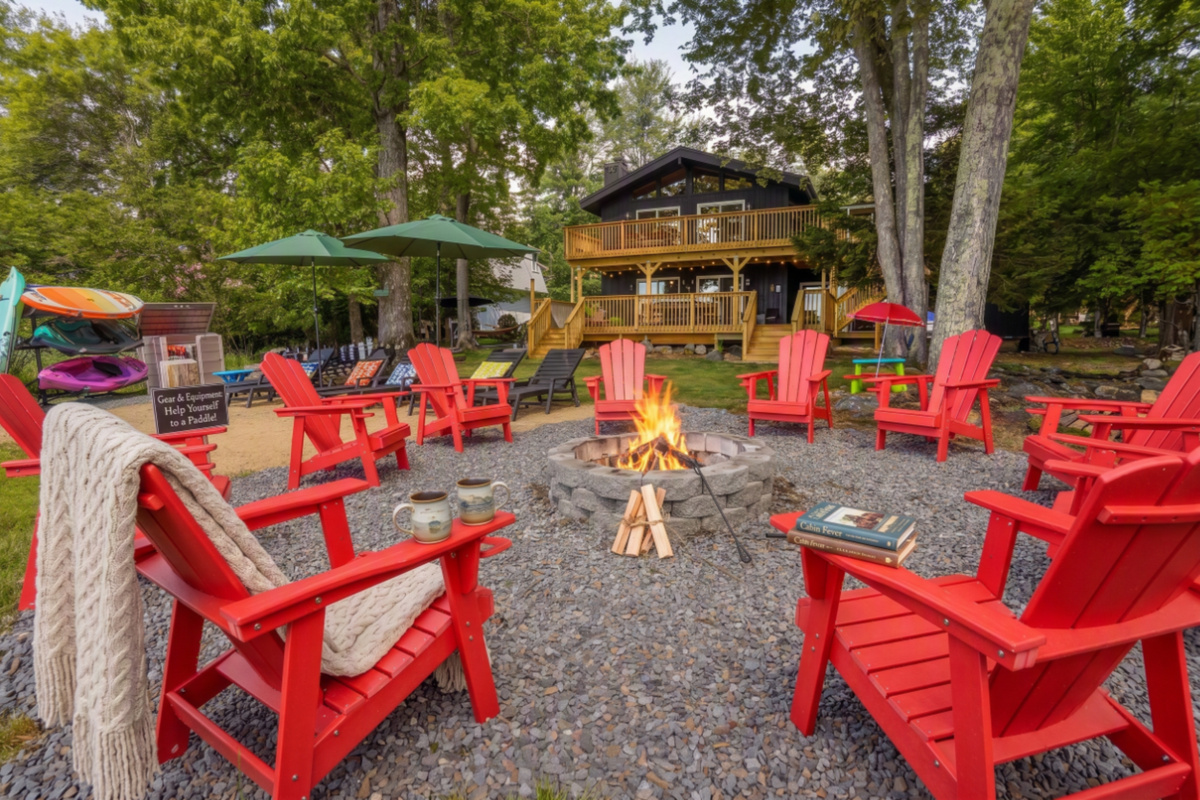 Lakeside fire pit surrounded by red Adirondack chairs — where the evenings happen