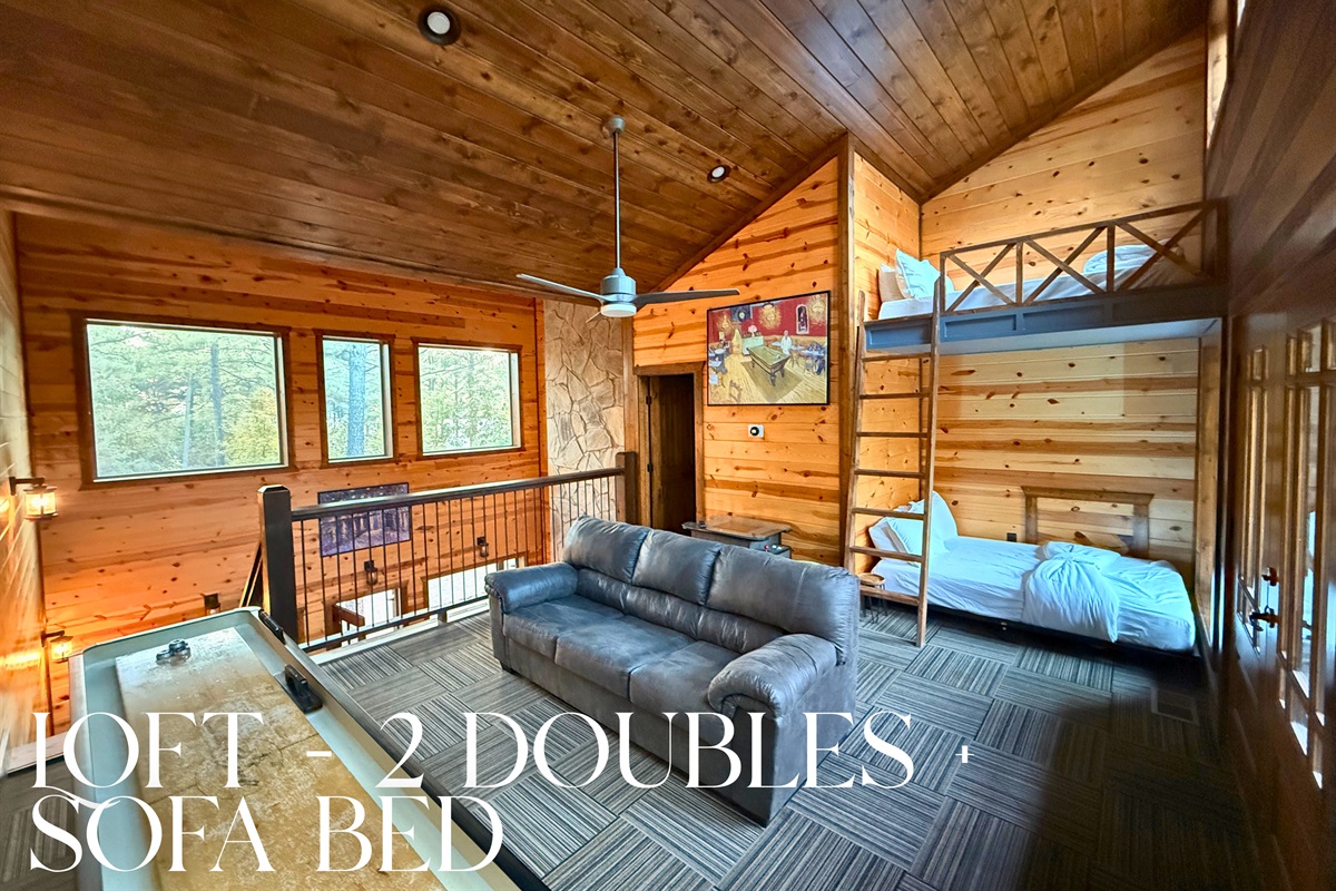 Cozy loft with vaulted wood ceiling and large windows offering scenic views.