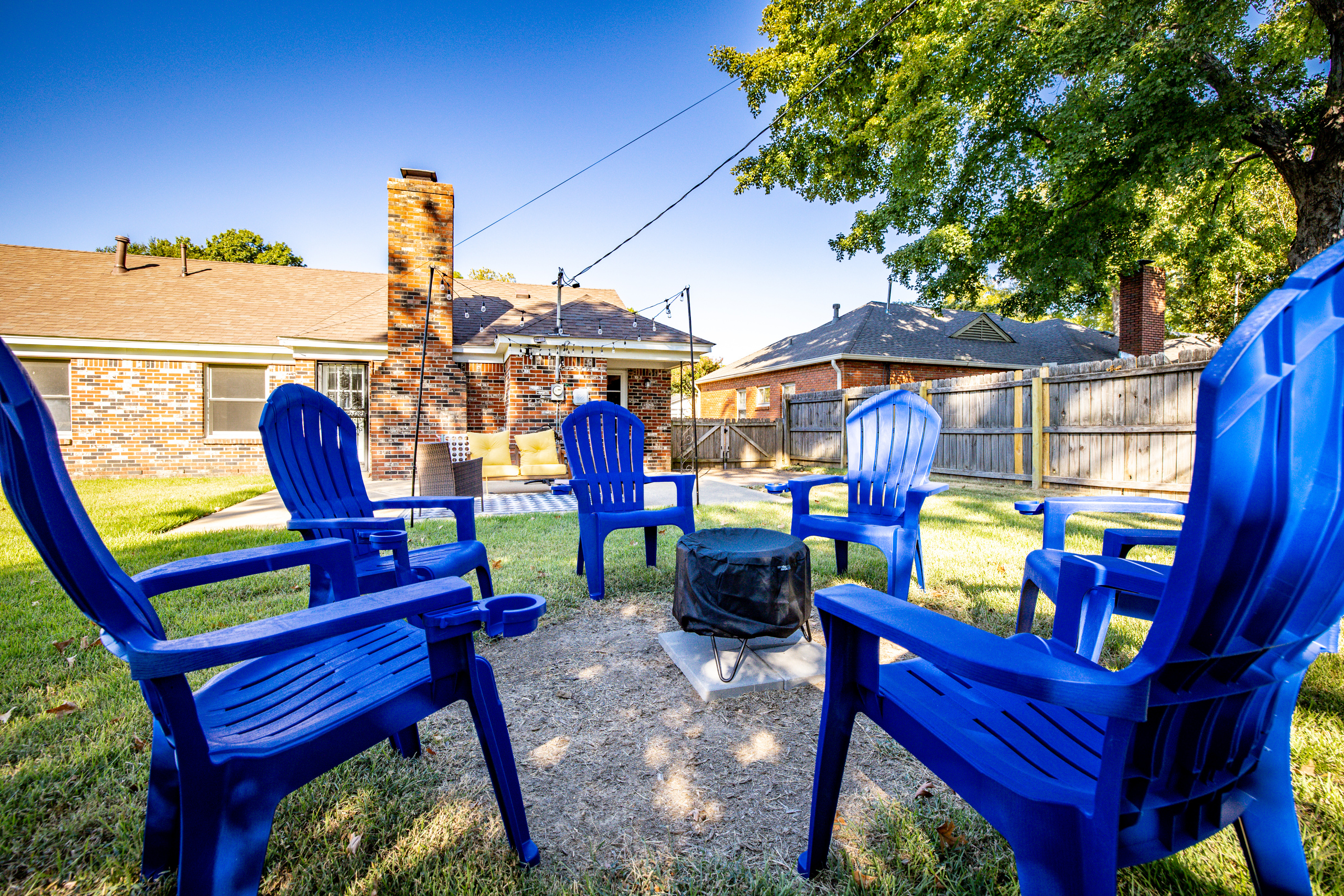 Fenced backyard with string-lit patio, fire pit, and electric grill.