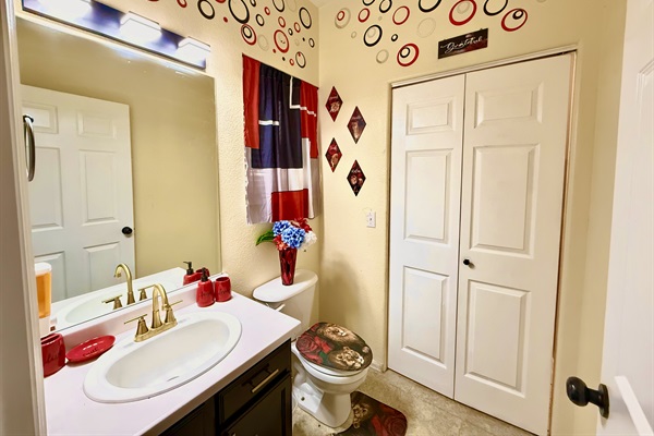 This stylish half bathroom offers a touch of luxury in a compact space. Adorned with red unique accent pieces, it’s the perfect spot for a quick freshen-up. Plus, with convenient access to the laundry room, you can easily keep your clothes fresh and tidy.