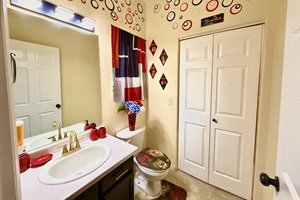This stylish half bathroom offers a touch of luxury in a compact space. Adorned with red unique accent pieces, it’s the perfect spot for a quick freshen-up. Plus, with convenient access to the laundry room, you can easily keep your clothes fresh and tidy.