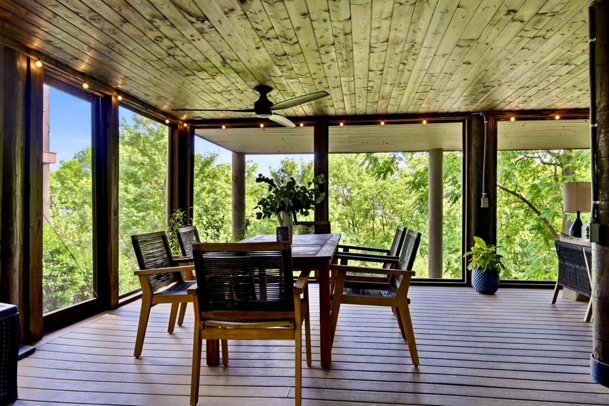 Breezy screened dining porch w/ wood table, ceiling fan & lush green views on every side.
