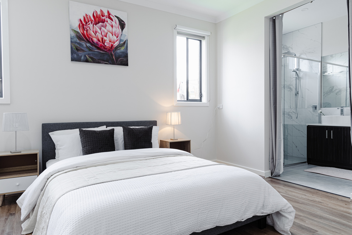 Bedroom with ensuite access, bed, bedside tables, lamps and artwork.