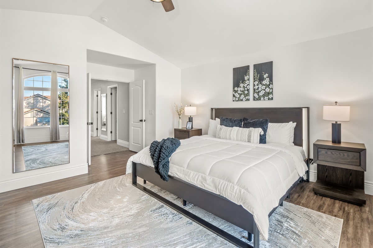 Spacious and light-filled primary bedroom featuring vaulted ceilings, a king bed, mounted TV, and a private en-suite bath. The oversized layout offers room to relax, unwind, and enjoy a true retreat feel during your stay.