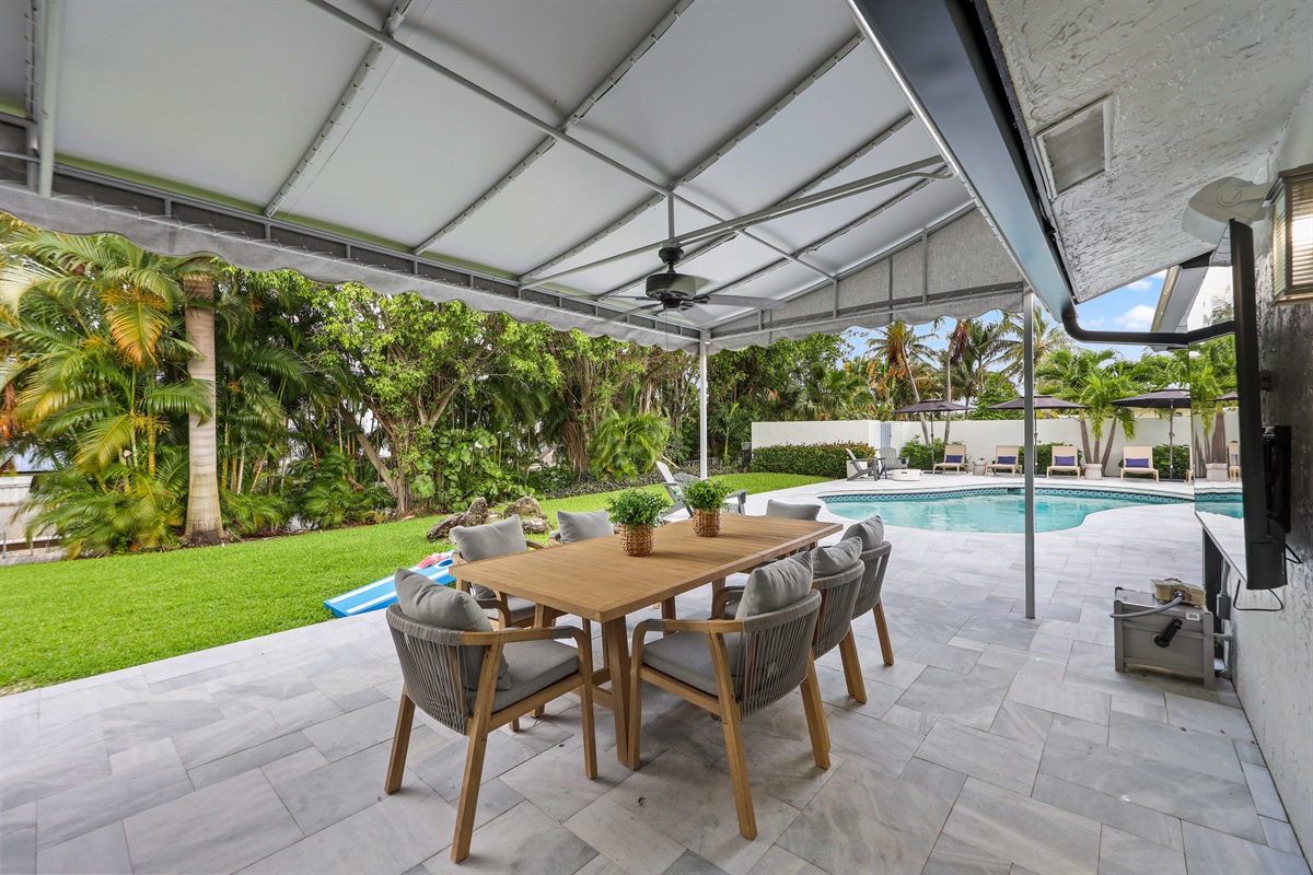Dine, grill, watch TV, or play cornhole from this covered outdoor hub overlooking the pool and tropical backyard.