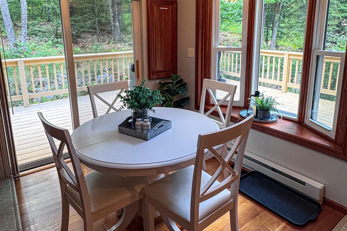 Dining table next to propane fireplace with walk out slider doors and large windows brings in light and wooded views