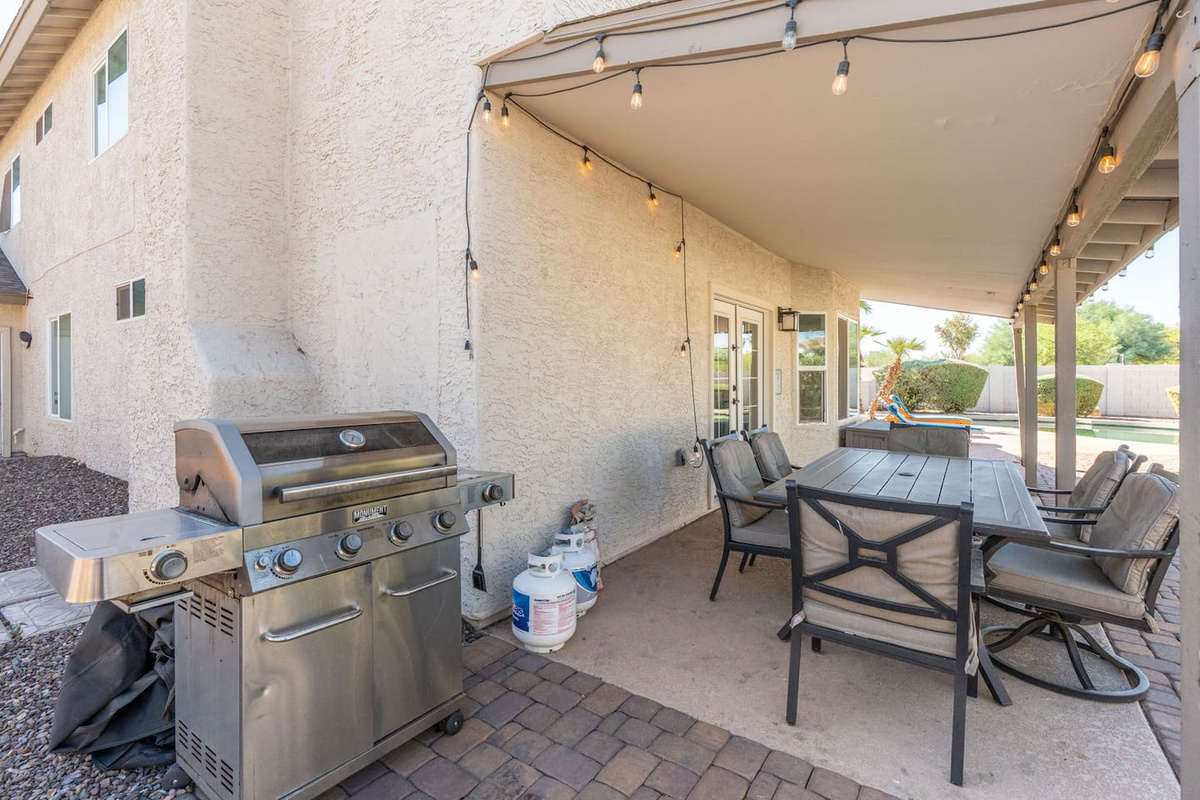 Outdoor kitchen and dining area with gas grill, covered patio, and pool views—ideal for entertaining.