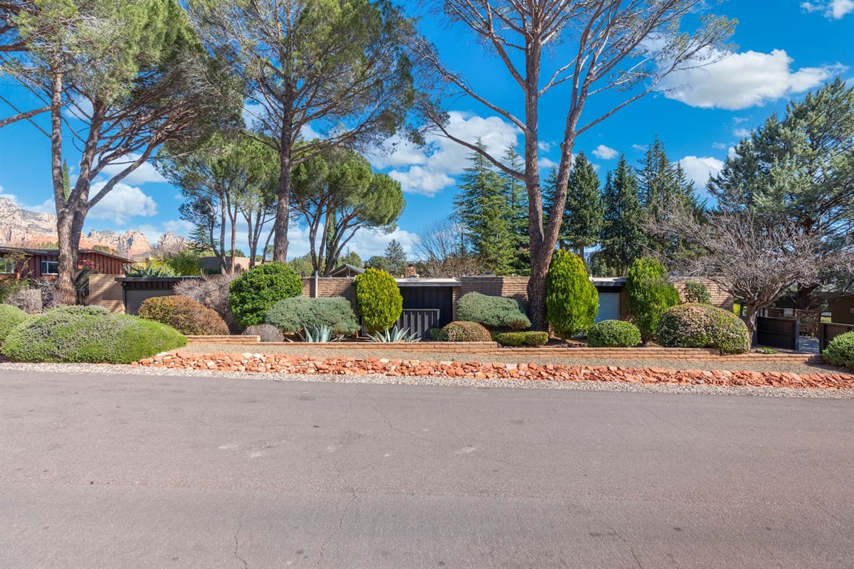 Beautifully landscaped frontage with mature trees, desert greenery, and classic Sedona red rock accents — private, serene, and perfectly maintained.
