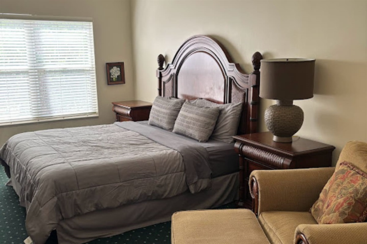 Comfortable bedroom with a large bed, cozy chair, bedside lighting, and plenty of natural light.