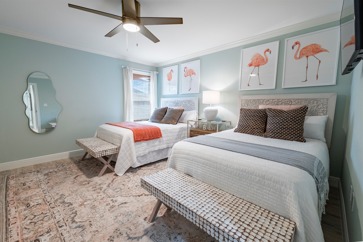 Charming twin bedroom with flamingo wall art, cozy beds, stylish decor, and soft lighting.
