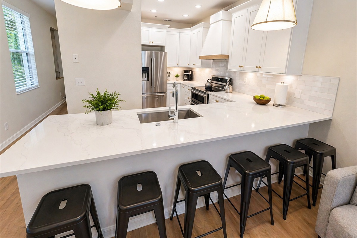 Modern, fully equipped kitchen with sleek white cabinetry, stainless steel appliances, and a spacious island with bar seating—perfect for cooking, dining, or entertaining. Bright lighting and an open layout make it the heart of the home.