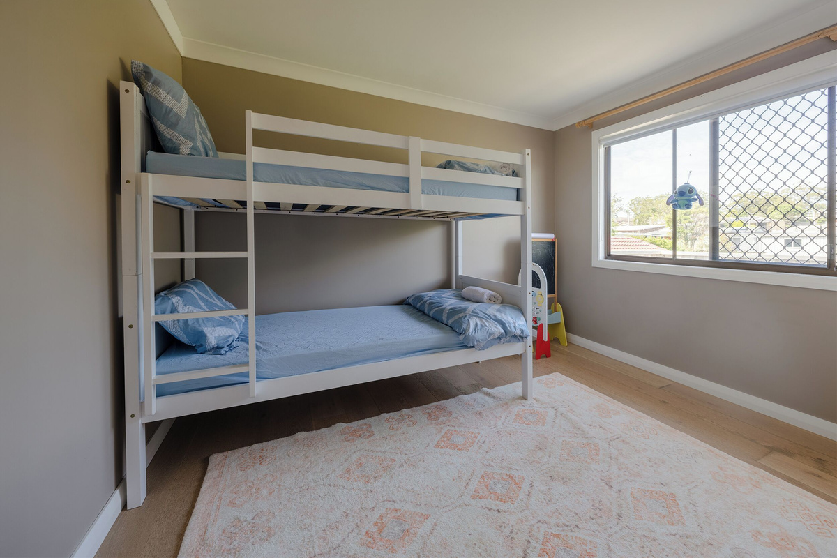 This bunk bedroom at Luna’s Sanctuary features two single bunks, timber floors, ceiling fan and a wide window with natural light.