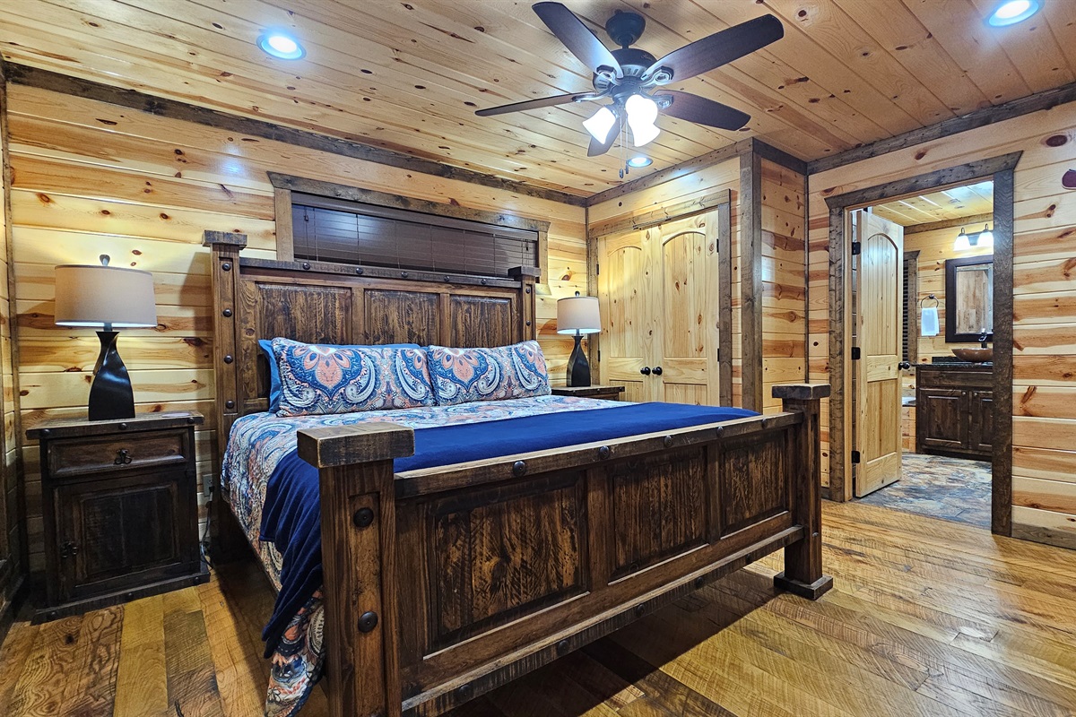 Bedroom 1: Relax in rustic charm with a plush bed and nature views through sunny windows!