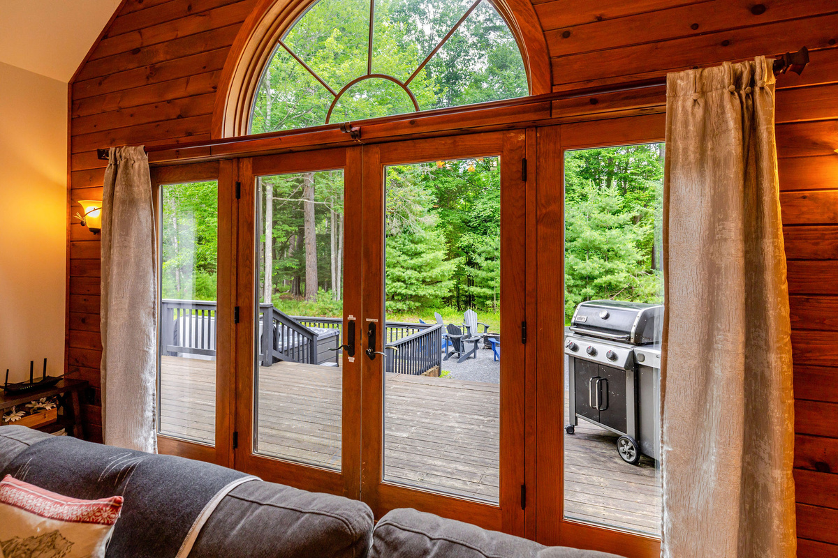 Step through the grand glass doors to the spacious deck, where you'll find a gas grill, hot tub, Adirondack seating, and peaceful woodland views—the perfect setting for outdoor dining and relaxing.
