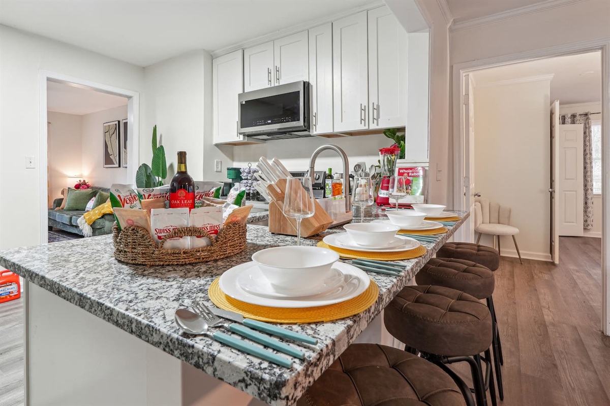 A fully equipped kitchen with a refrigerator, microwave, stove, oven, dishwasher, coffee maker, kettle, toaster, and blender. Includes plates, bowls, utensils, pots, and pans, plus four bar chairs for casual dining or socializing.
