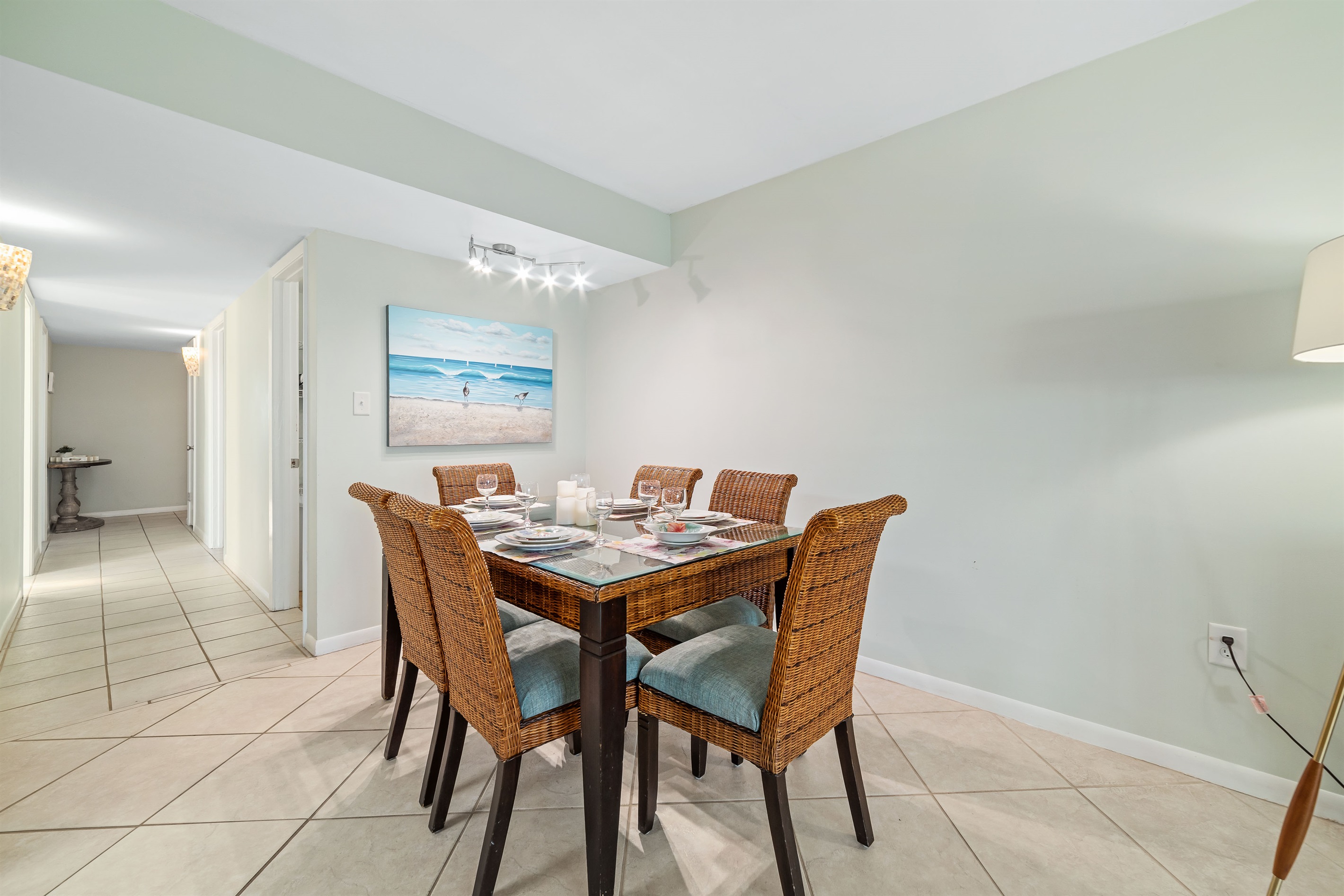 This dining area features a glass-top table with wicker chairs, set with place settings and glassware, creating a welcoming space for shared meals.