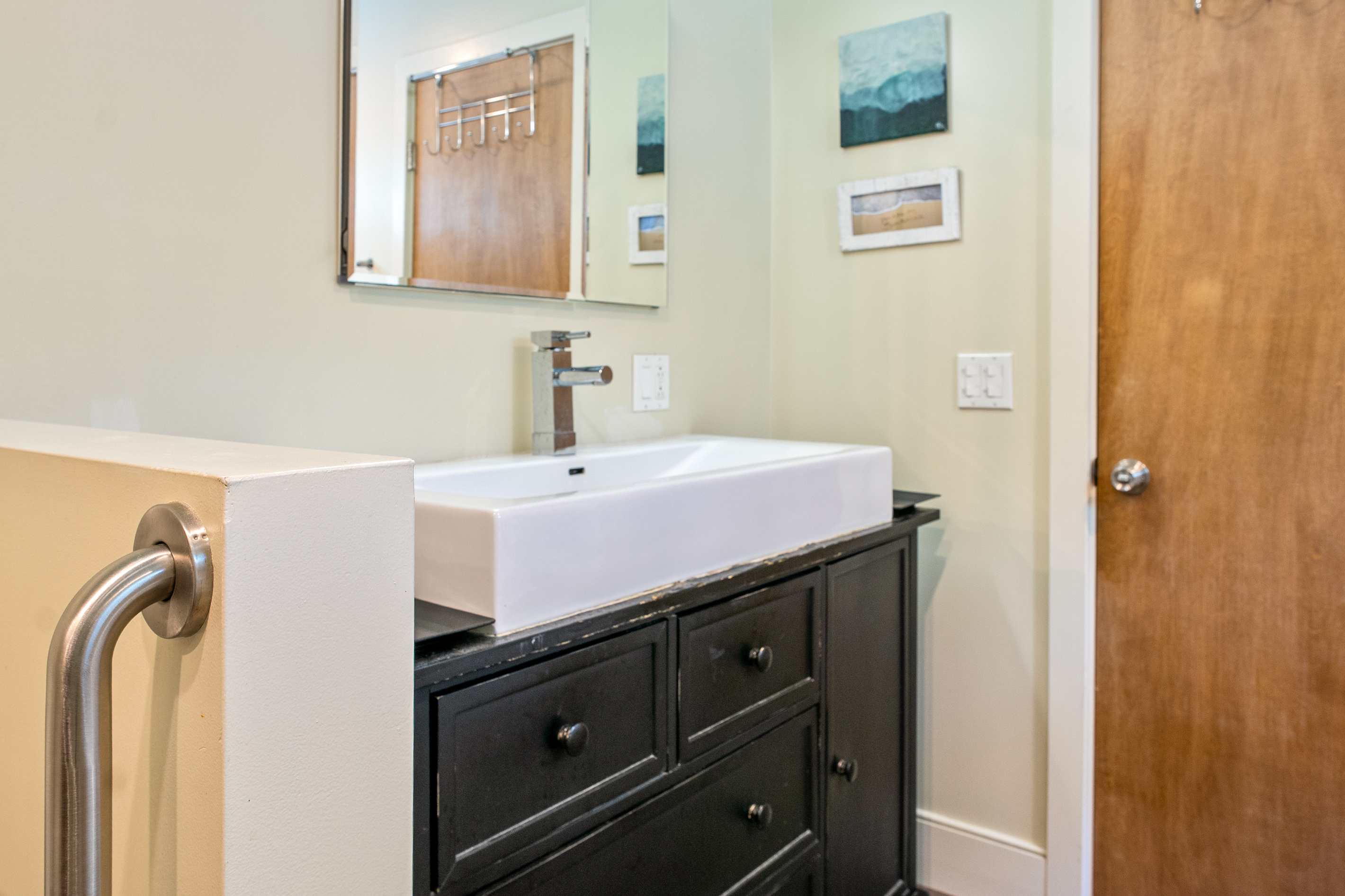Sleek vanity area at "The Crag." The primary en-suite features a large porcelain vessel sink, single-lever modern faucet, dark wood vanity cabinet, frameless mirror, and integrated safety grab bars for added comfort.