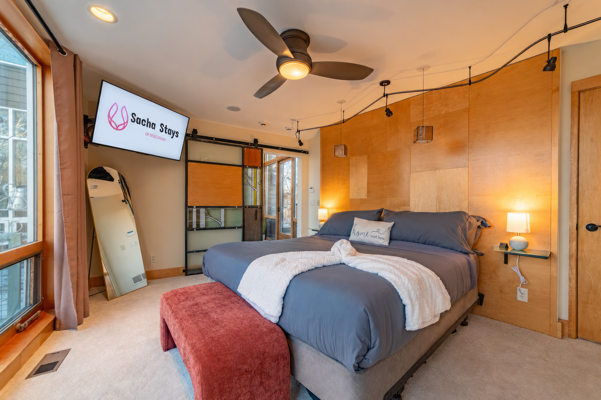 The main level master suite features a luxury King bed, 50" smart TV, floor to ceiling windows, en suite closet and bathroom with tub, dual rain shower, dual vanity, and heated floors
