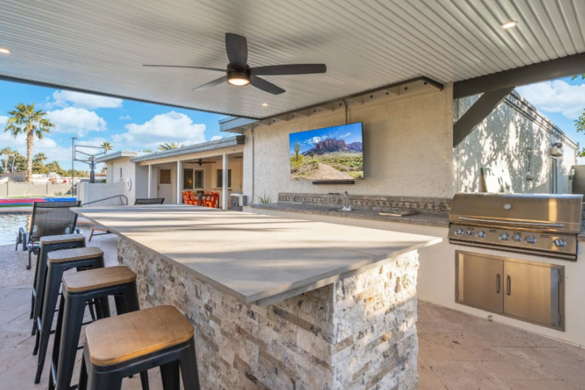 Bar stools line the outdoor kitchen, with a mounted TV keeping the group entertained while the grill does its work.
